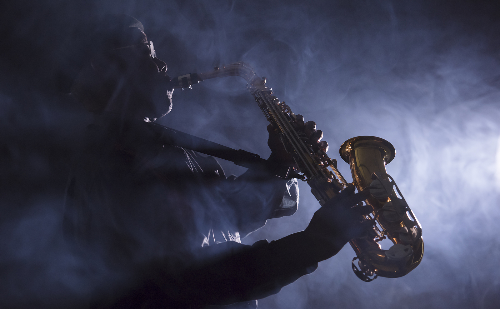 African American jazz musician playing the saxophone through smokey light in club